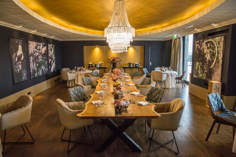 Ein stilvoller Speisesaal mit einer langen, gedeckten Tafel unter einem glanzvollen Kronleuchter, umgeben von eleganten Stühlen und dekorativen Bildern an der Wand.