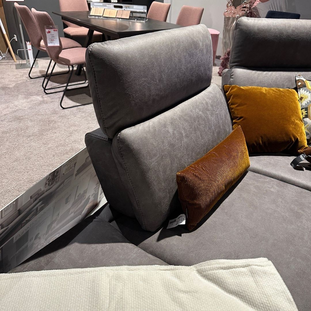 Graue Couch mit orangefarbenen Kissen in einem eleganten Wohnzimmer mit Esstisch im Hintergrund