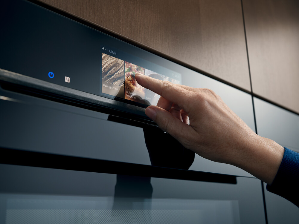 Hand bedient den Touchscreen eines modernen Backofens mit verschiedenen Einstellungen