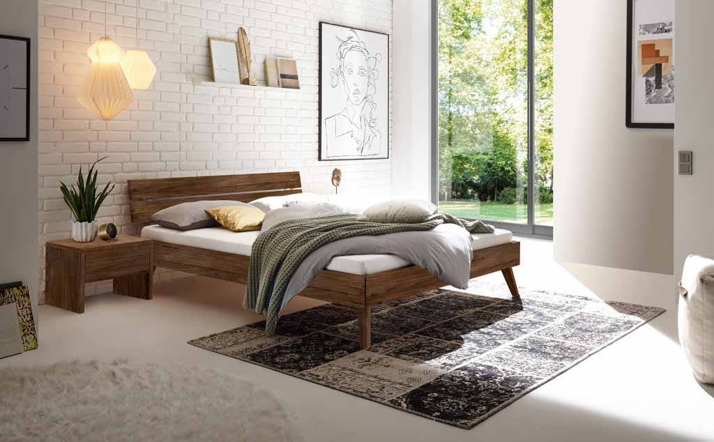 Hasena Trento - Bett Ortona | Nussbaum, geölt Ein stilvolles Schlafzimmer mit einem Holzbett, Nachttisch, Wanddekorationen und einer großen Fensterfront, die Tageslicht hereinlässt.