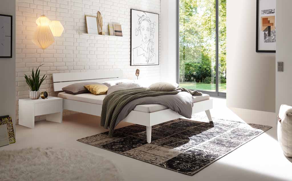 Hasena Trento - Bett Ortona | Buche weiß, deckend lackiert Helles Schlafzimmer mit modernem Bett, Nachttisch und dekorativem Wandbild, Tageslicht flutet durch große Fenster.