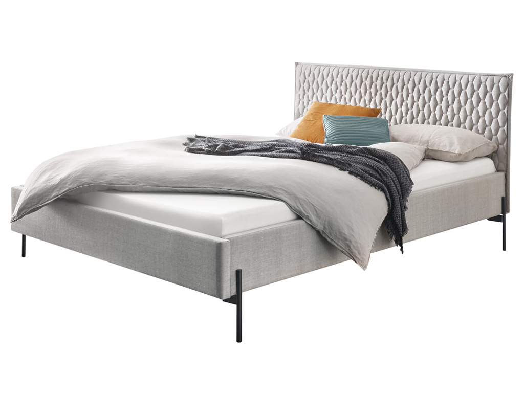 Ein vollständig aufgebautes Bettmodell Gloria mit grauem Stoffbezug und einem auffälligen, gesteppten Kopfteil, präsentiert in einem minimalistischen Stil.