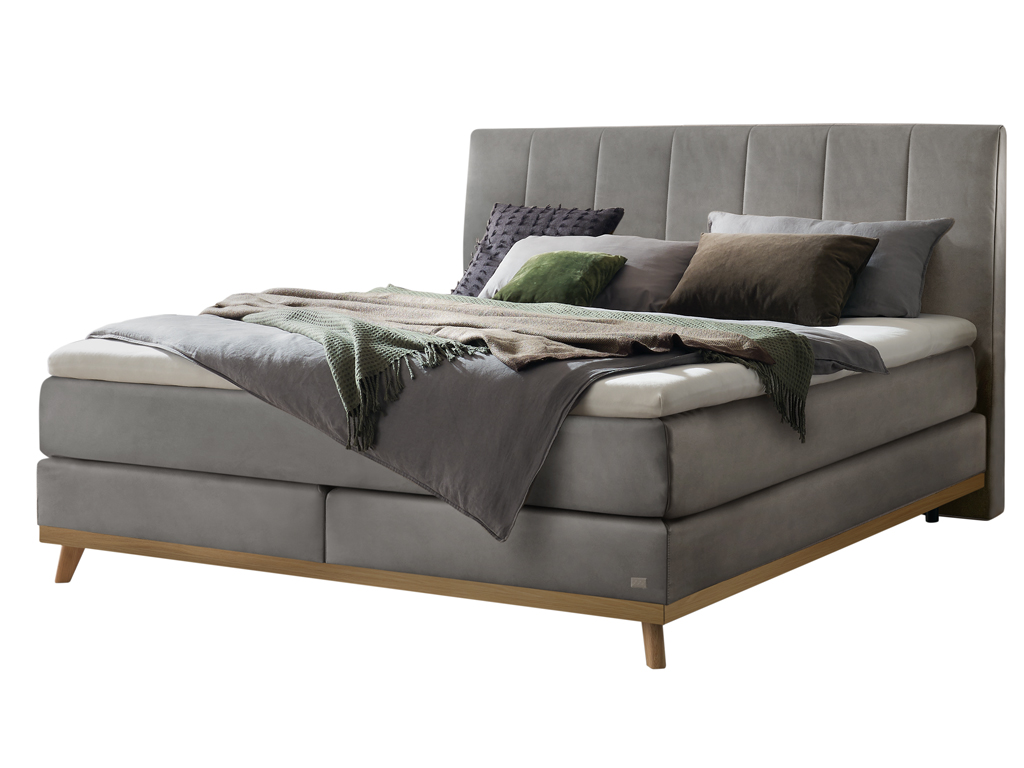 Ein freigestelltes Produktfoto des Hasena Boxspringbettes Pronto Stefania mit einem stahlgrauen Stoffbezug, dekoriert mit Kissen und einer Decke.