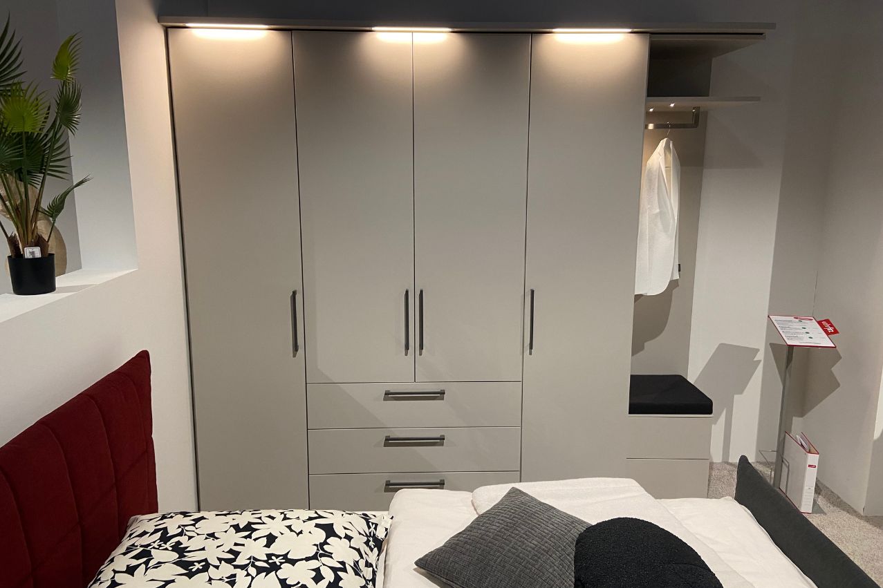 Loddenkemper - MAXX | Kleiderschrank 4-teilig Grauer Kleiderschrank mit Schubladen und Hängemöglichkeiten, beleuchtet, neben einem Bett mit dekorativen Kissen