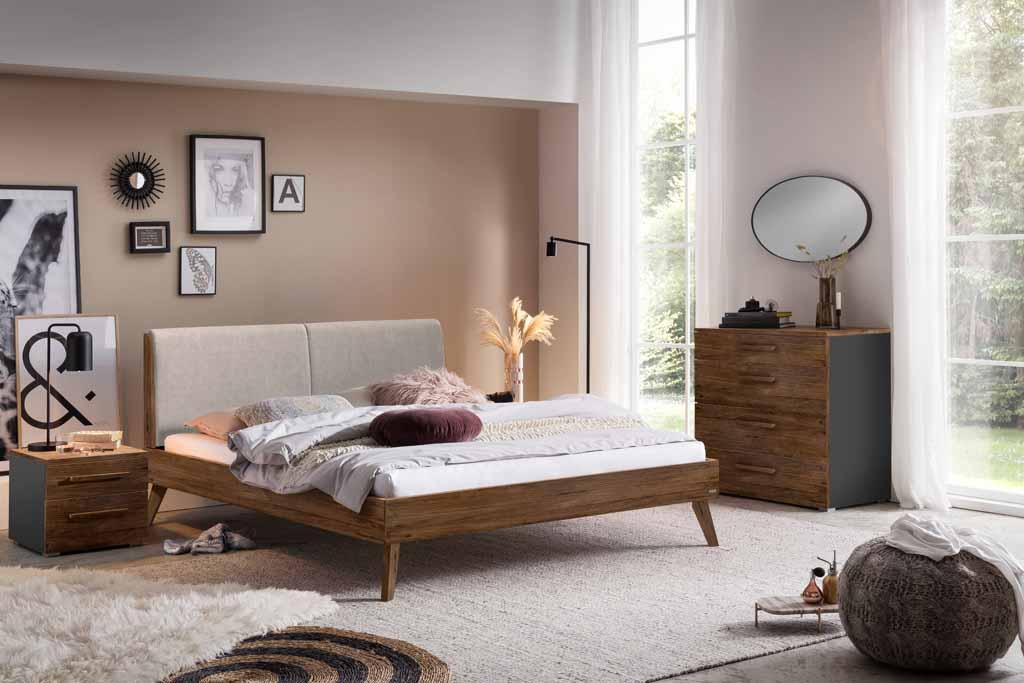 Schlafzimmer mit modernem Holzbett, Nachttisch und Kommode, dekoriert mit Bildern und Pflanzen, in einem hellen Raum mit großen Fenstern.