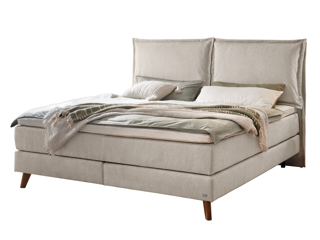 Ein Hasena Boxspringbett Pronto Ricarda mit hellgrauem Stoffbezug, das mit Decke und Kissen dekoriert ist.