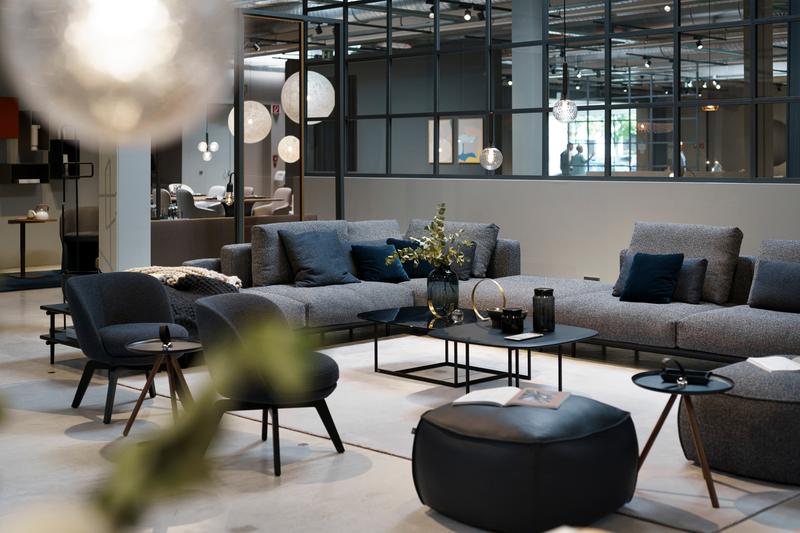 Wohnzimmereinrichtung mit unterschiedlichen Polstermöbeln in dunkelgrau und schwarz ein Couchtisch mit Glas Tischplatte steht in der Mitte