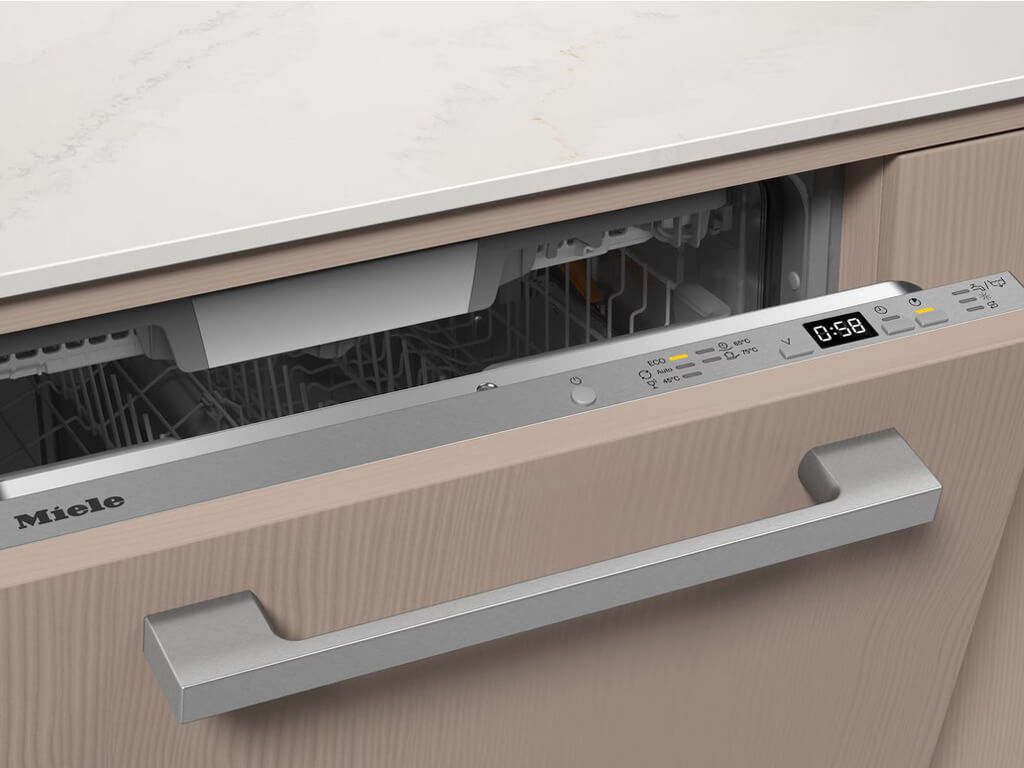 Nahaufnahme des oberen Bereichs eines geöffneten Miele Geschirrspülers, der in eine Küchenzeile mit heller Holzfront integriert ist.