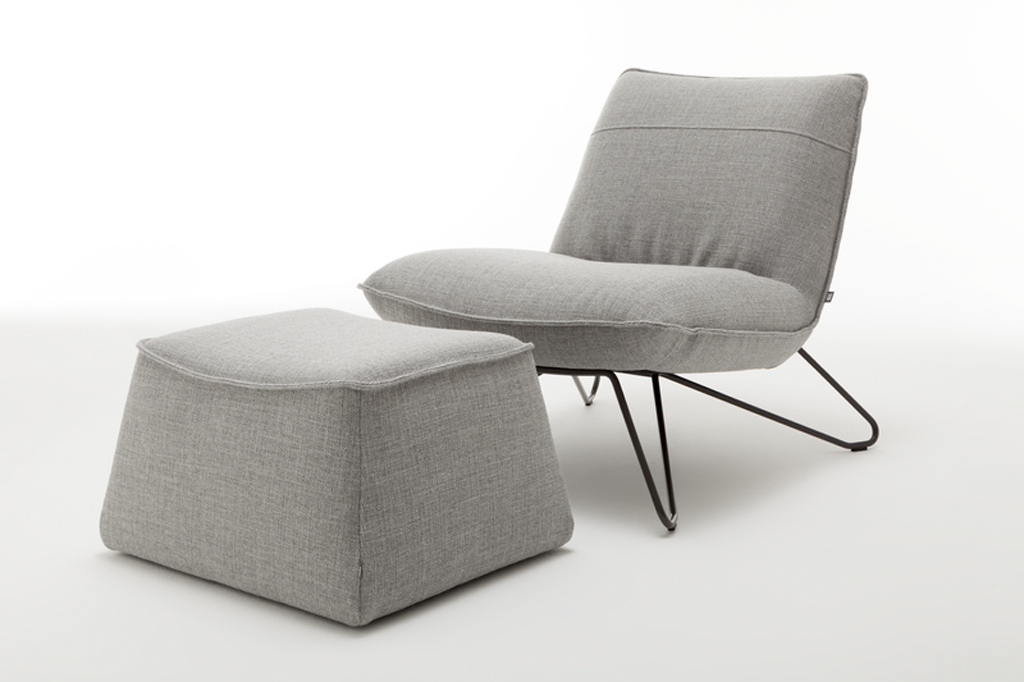 grauer designersessel mit schwarzen metallgestell und polsterhocker vor weißem Hintergrund