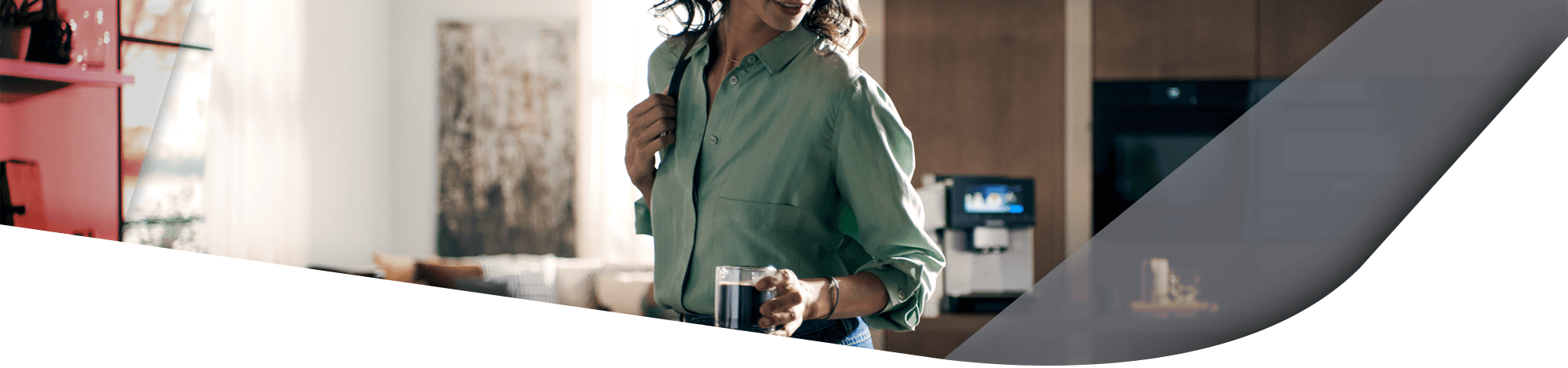 Eine Frau läuft in Ihrer Küche mit einem Kaffee in der Hand und ist sorgenlos, da Sie eine 5-jährige Garantie für Ihre Elektrogeräte abgeschlossen hat. 