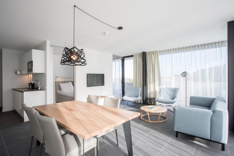 Esszimmer mit Holztisch und zwei Polsterstühlen in beige. Blick in das Wohnzimmer mit hellblauen Polstermöbeln