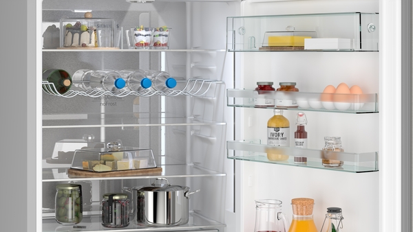 Der geöffnete Kühlschrank zeigt verschiedene Lebensmittel, darunter Eier, Getränke, Käse und Gläser auf den Regalen.