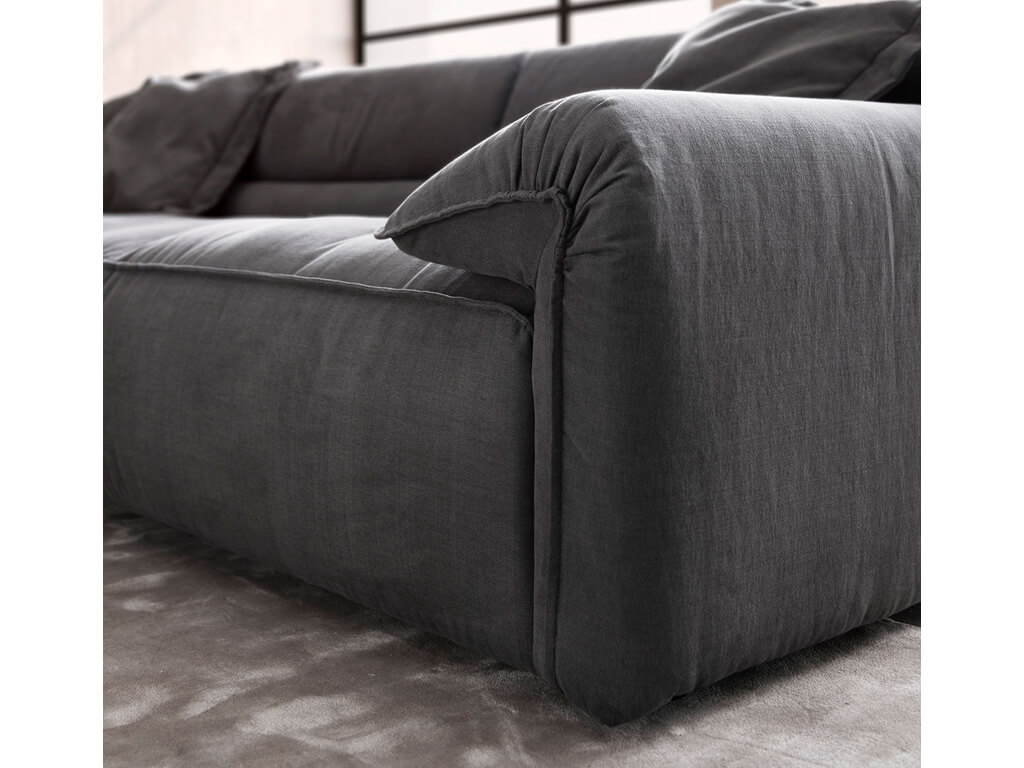 Nahaufnahme der Armlehne und des Rückens eines cremefarbenen Ledersofas, mit einem modernen Beistelltisch mit Vasen im Vordergrund und einem Fensterblick auf ein Gewässer und Hügel im Hintergrund.