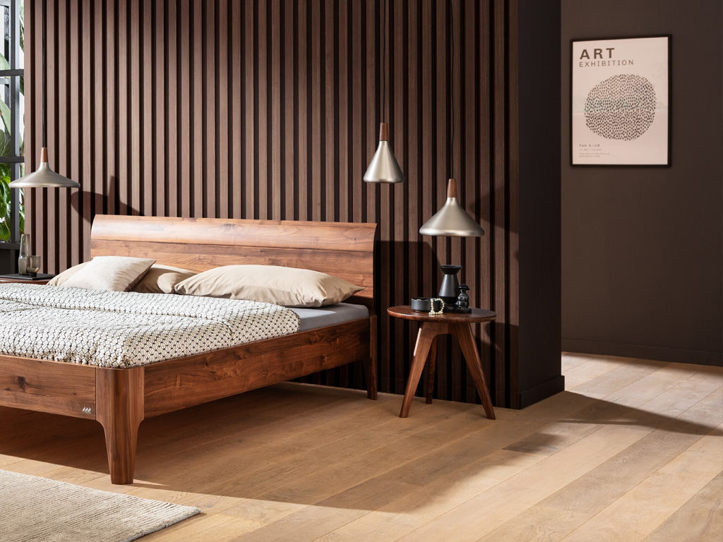 Braunes Holzbett mit braunem runden Beistelltisch auf drei Beinen an einem Bett vor einer modernen Wand mit Holzlamellen in einem modernen zimmer stilvoll dekoriert Circo von Hasena