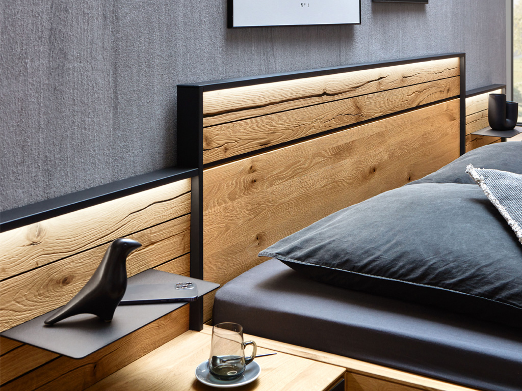 Nahaufnahme eines eleganten Holz-Bettgestells mit integrierter Beleuchtung und stilvollen Accessoires