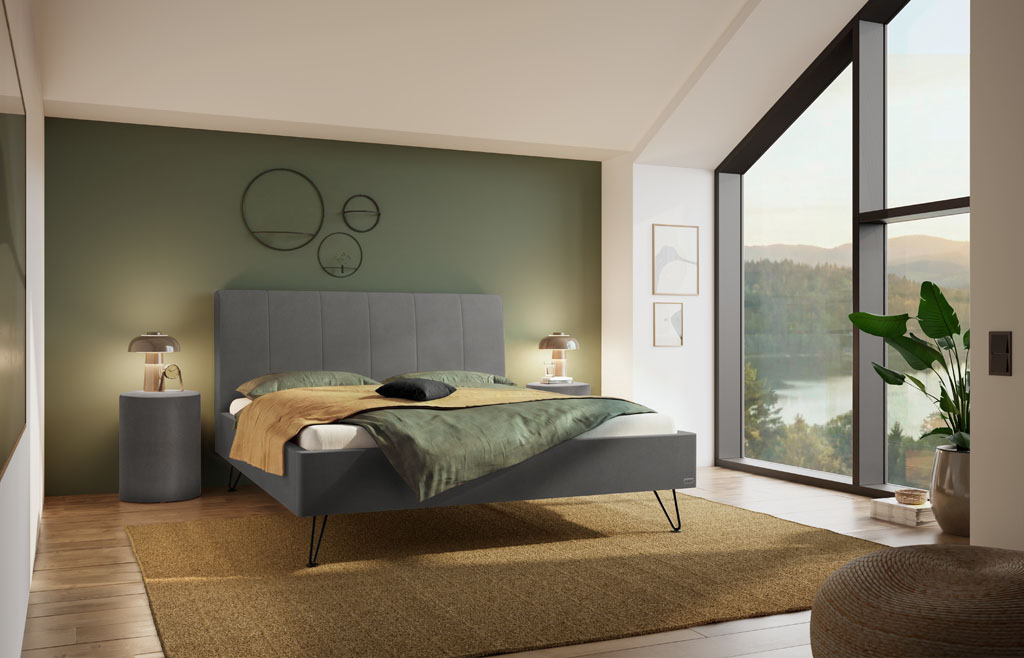 Graues Polsterbett mit vertikal gestepptem Kopfteil und schwarzen Metallfüßen in einem modernen Schlafzimmer mit grüner Wand und großer Fensterfront (KI-generiert)