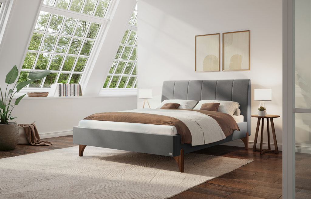Graues Polsterbett mit vertikal gestepptem Kopfteil und geölten Nussbaum-Holzfüßen in einem modernen Schlafzimmer mit Dachschräge und großem Fenster (KI-generiert)