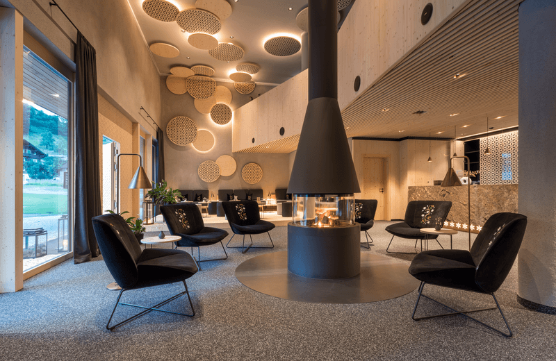 Innenbereich einer modernen Lounge mit einem zentralen Kamin, eleganten schwarzen Sesseln und kreativen Deckenelementen