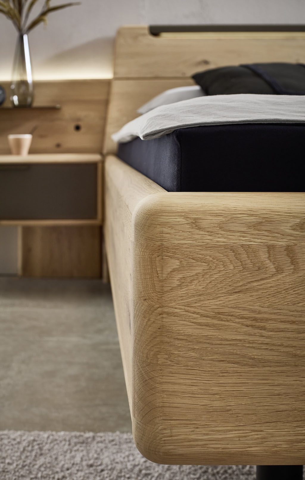 Detailaufnahme einer Holzbettkante im Hintergrund mit einem Konsolennachttisch mit Paneelbeleuchtung
