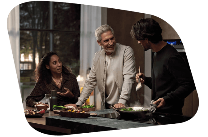 Drei Personen sitzen zusammen an einem Tisch, welche gemeinsam essen & lachen.