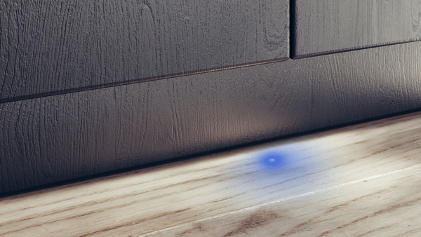 Detailaufnahme des Bodens vor einem geschlossenen, in eine dunkle Küche integrierten Geschirrspüler. Ein blauer Lichtpunkt (InfoLight/TimeLight) projiziert auf den Holzboden, der den Betriebsstatus anzeigt.