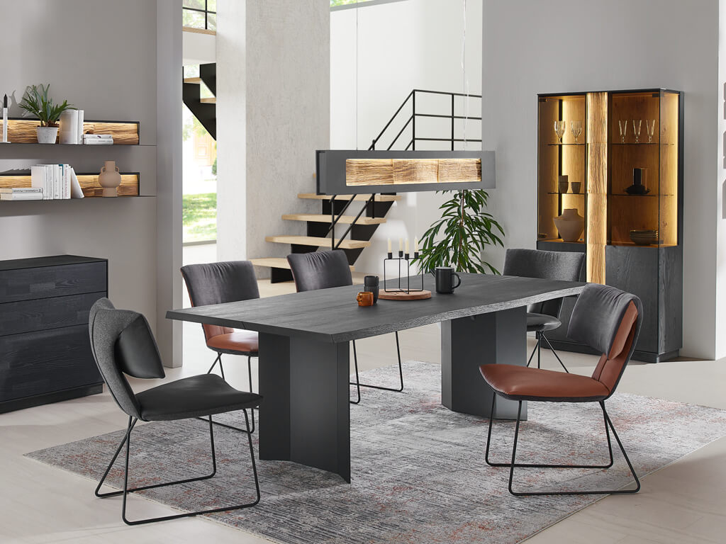 Ein elegant gestalteter Essbereich mit einem großen Holztisch und verschiedenen Stühlen in einem modernen Raum mit dekorativen Regalen und einem beleuchteten Schrank.