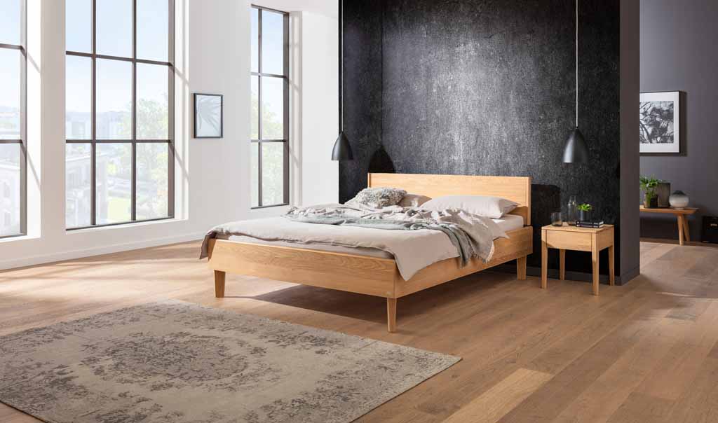 Hasena Wood-Line Bett | Eiche bright, geölt Ein stilvolles Schlafzimmer mit Holzbett, Nachttisch, großer Fensterfront und elegantem Teppich auf Holzboden