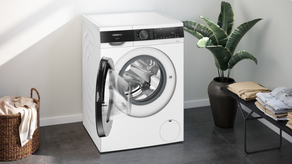 Eine energieeffiziente Waschmaschine mit geöffneter Tür in einem elegant eingerichteten Raum mit Pflanzen und gefalteter Wäsche