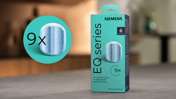 Die türkisfarbene Siemens EQ series Verpackung steht auf einer Küchenarbeitsplatte. Ein kreisförmiges Icon hebt das Symbol „9x“ hervor und zeigt die detaillierte Struktur einer blau-weißen Entkalkungstablette.