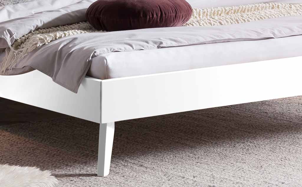 Nahaufnahme eines modernen weißen Bettgestells mit grauer Bettwäsche und braunem Kissen auf einem Teppich