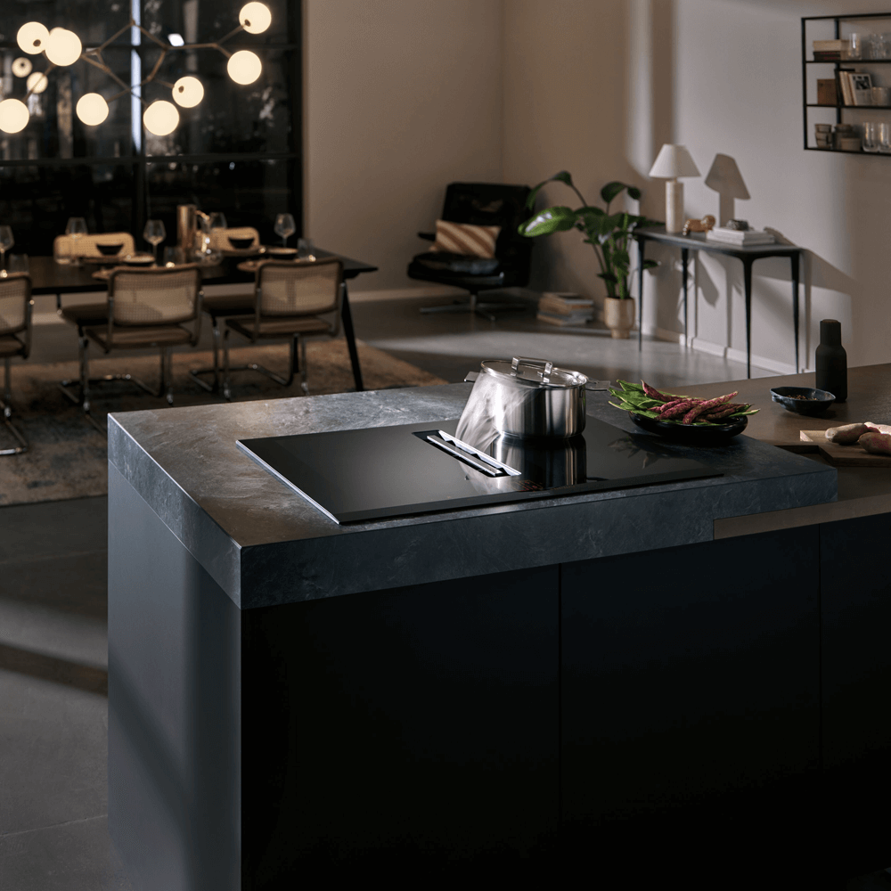 Eine stilvolle Küchenszene mit einer modernen Kochinsel aus dunklem Marmor, auf der ein Topf steht. Im Hintergrund ist ein Essbereich mit einem gedeckten Tisch und Designerstühlen sichtbar.