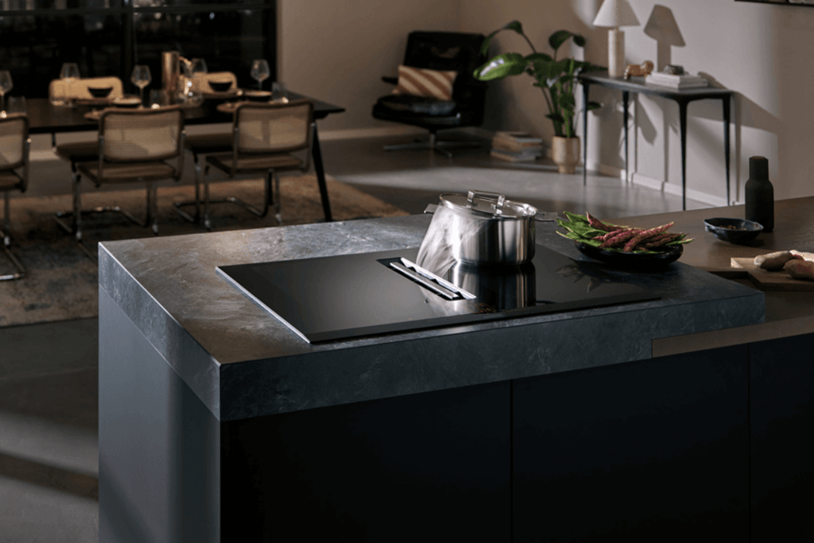Eine stilvolle Küchenszene mit einer modernen Kochinsel aus dunklem Marmor, auf der ein Topf steht. Im Hintergrund ist ein Essbereich mit einem gedeckten Tisch und Designerstühlen sichtbar.