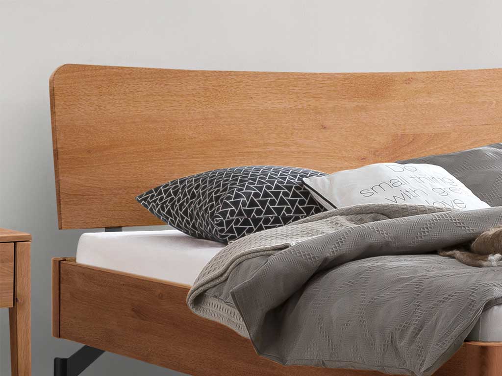 Ausschnitt von einem braunem Holzbett mit Holzkopfteil und moderner Bettwäsche Hasena