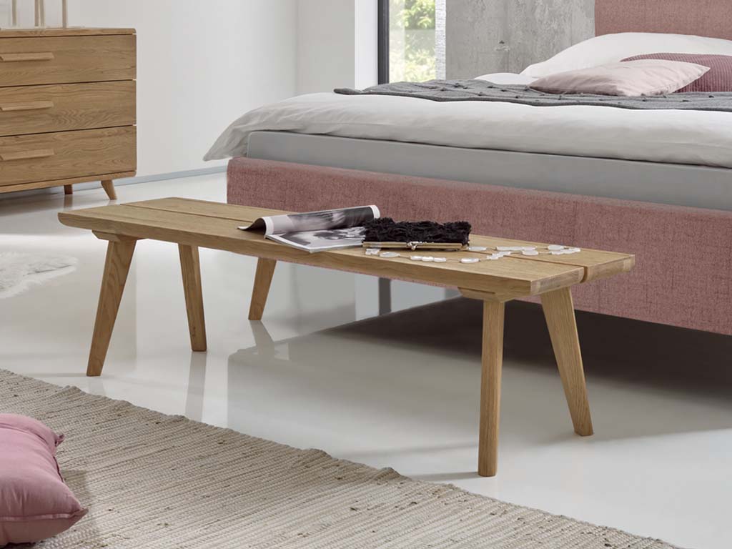 braune holzbank stilvoll dekoriert vor rosafarbenem polsterbett und in einem modernen zimmer