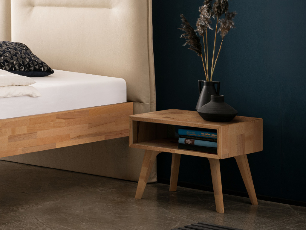 hellbrauner Nachttisch auf vier hohen beinen und in form eines offenen faches stilvoll dekoriert an einem bett stehend vor einer blauen wand jaca von hasena