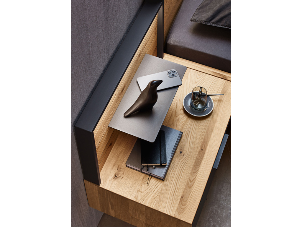 Ein stilvoll gestalteter Nachttisch aus Holz mit einem Laptop, einem Smartphone, einer Vogelstatue und einer Tasse Kaffee