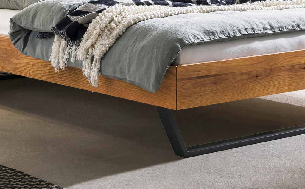 Detailansicht eines modernen Holzbetts mit Metallbeinen und grauer Bettwäsche im Zimmer