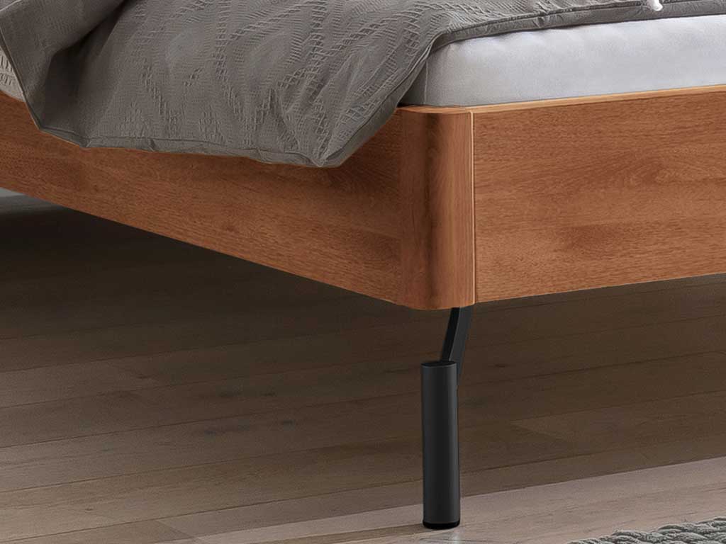 Ausschnitt von einem braunem Holzbett mit schwarzen Füßen und moderner Bettwäsche Hasena