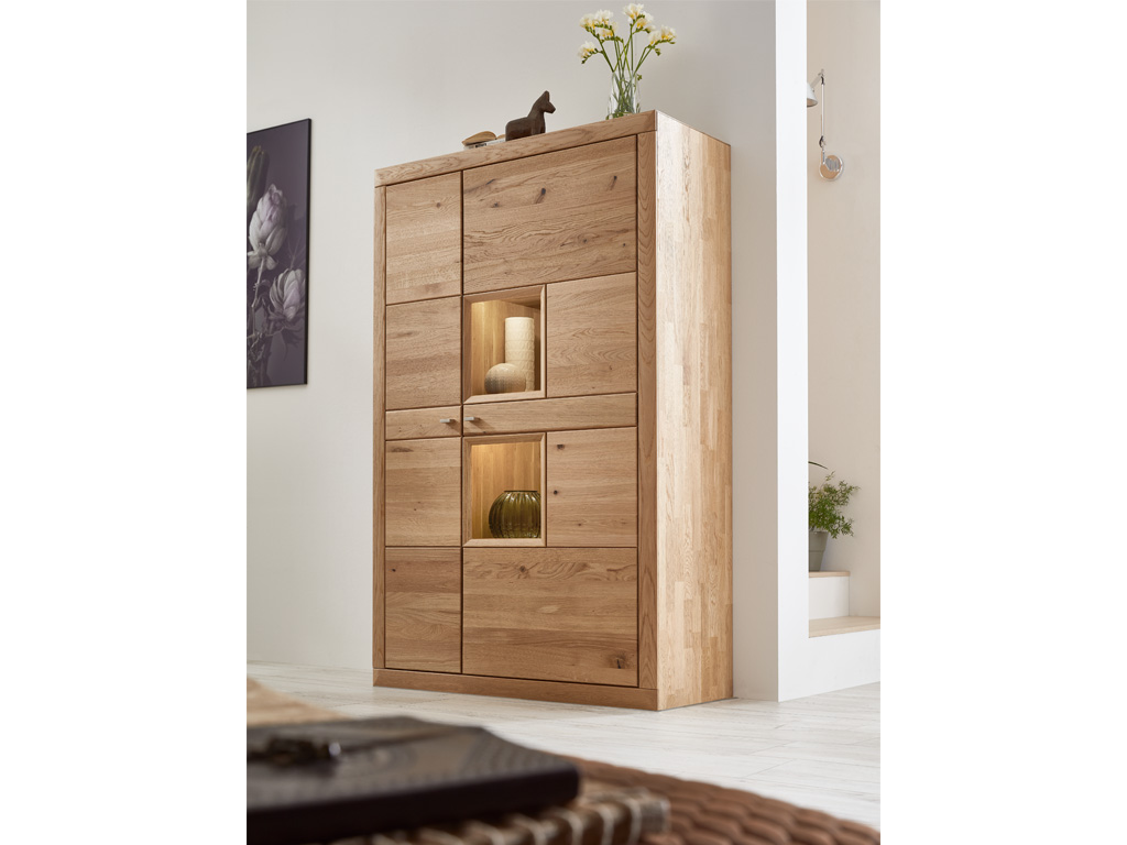 Wöstmann Aurum  - Vitrinenschrank | Type 4013/4014 | Wildeiche massiv | B: 108,2 cm | konfigurierbar Ein moderner Holzschrank mit eingebauten Leuchten in einem hellen Raum.