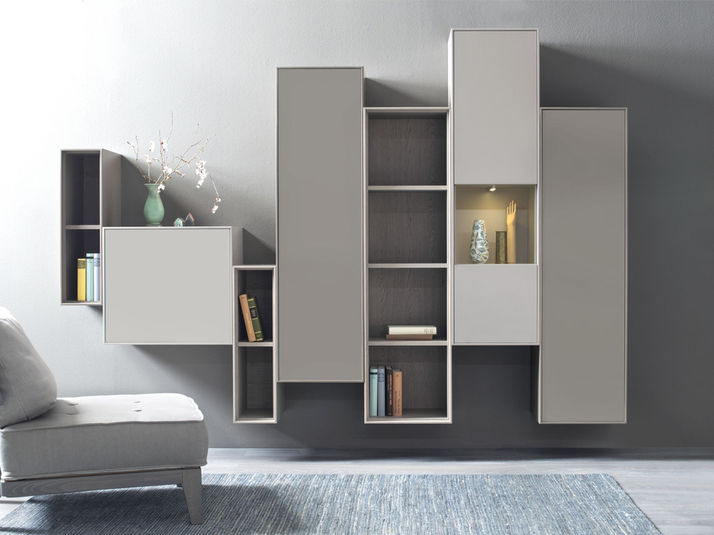 Sudbrock Game - Wohnwand | Eiche sahara furniert, Lack sienna, Lack terra | B: 260 cm Hängendes Regalsystem in modernem Design mit Büchern und Dekorationen, neben grauem Sessel auf blauem Teppich