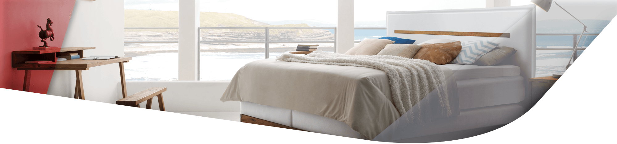 Harmonisches Bild eines Hasena Boxspringbettes in weiß mit Holzdetails vor einer Fensterfront mit Blick auf das Meer.