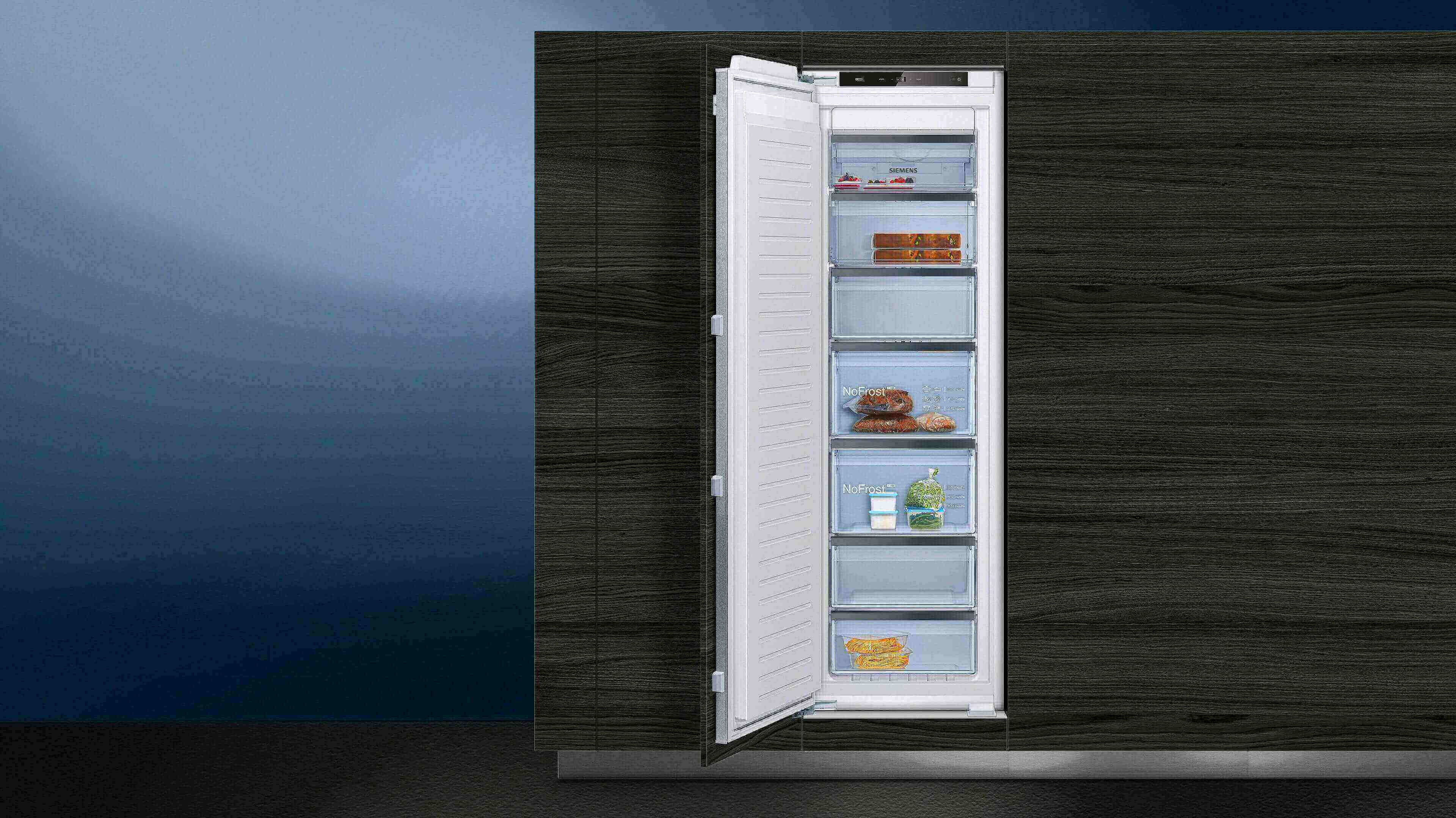 Eingebauter Siemens Einbau-Gefrierschrank mit geöffneter Tür in einer dunklen Holzküche, gefüllt mit verschiedenen tiefgekühlten Lebensmitteln.