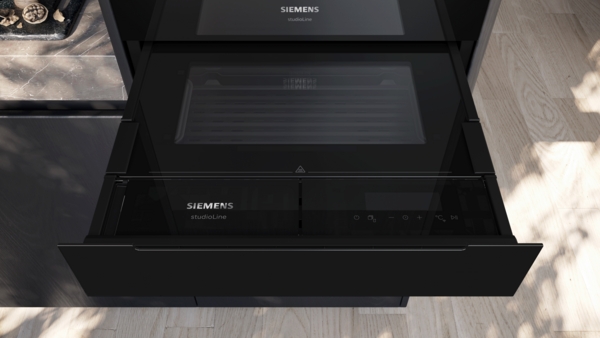 Detailaufnahme der Front des eingebauten Siemens StudioLine Küchengeräts. Im unteren Bereich ist eine geschlossene, schwarze Schublade mit Bedienelementen und dem StudioLine-Logo zu sehen, die unter einem weiteren, ebenfalls schwarzen Fach eingebaut ist.