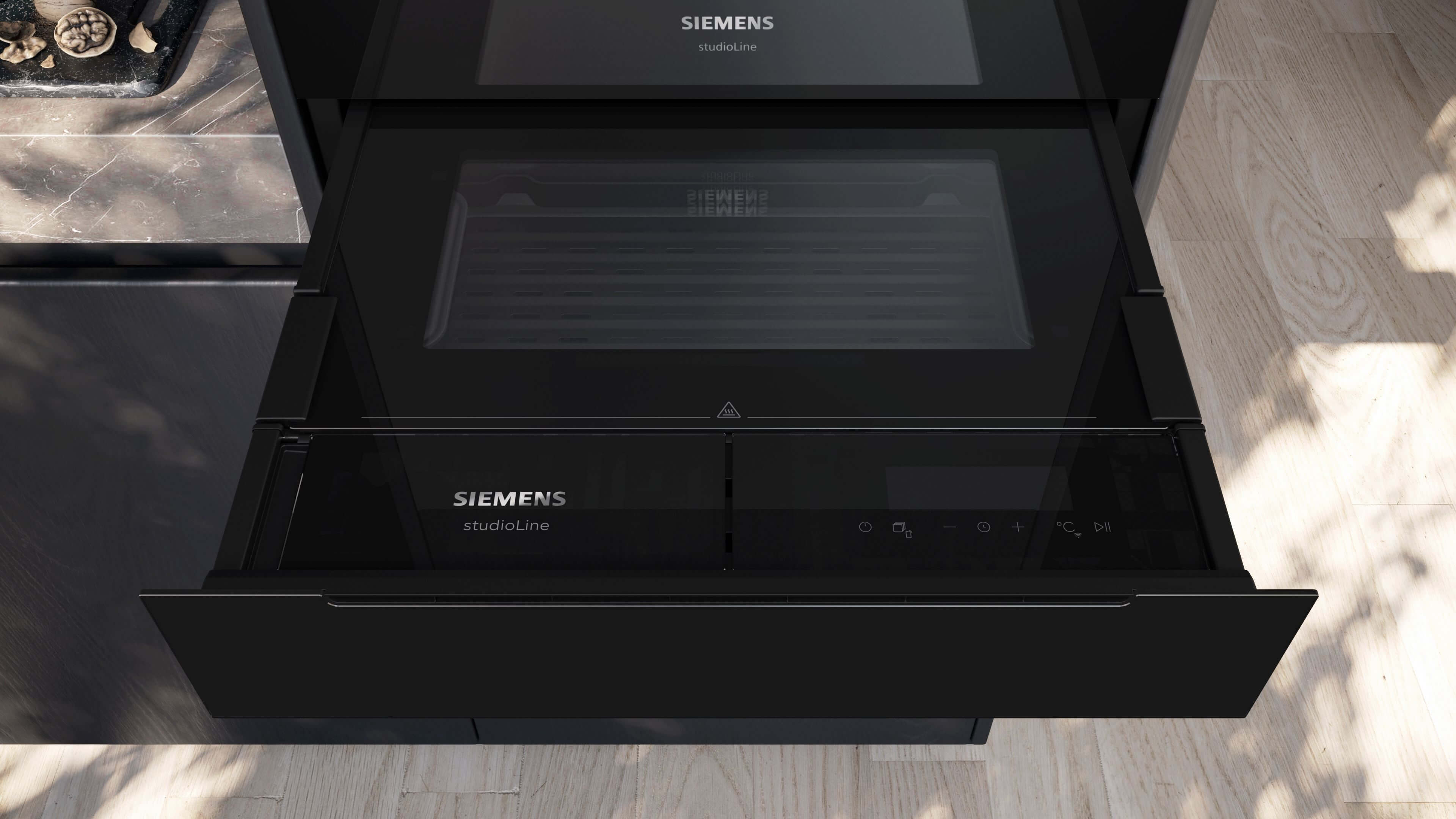 Detailaufnahme der Front des eingebauten Siemens StudioLine Küchengeräts. Im unteren Bereich ist eine geschlossene, schwarze Schublade mit Bedienelementen und dem StudioLine-Logo zu sehen, die unter einem weiteren, ebenfalls schwarzen Fach eingebaut ist.