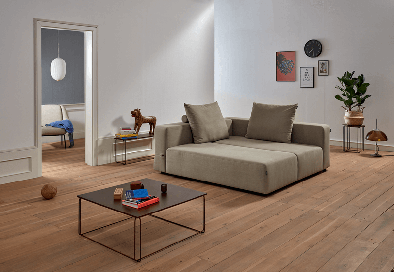 Ein stilvolles Wohnzimmer mit einem beigen Sofa, Holzboden, Couchtisch und Pflanzen. Kunstwerke schmücken die Wand.