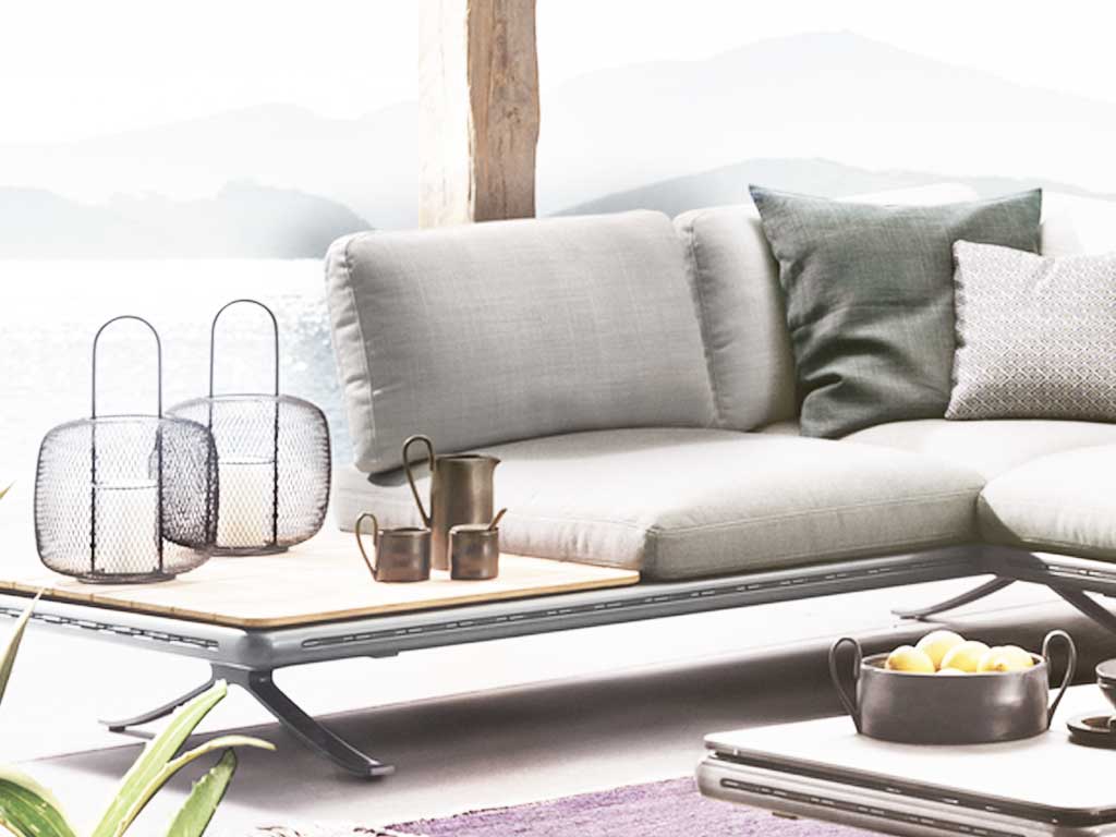 Rolf Benz Yoko 219 - Rückenkissen Eine stilvolle Gartenlounge mit einem modernen grauen Sofa, dekorativen Kissen und einem Tisch mit Körben und Geschirr im Freien.