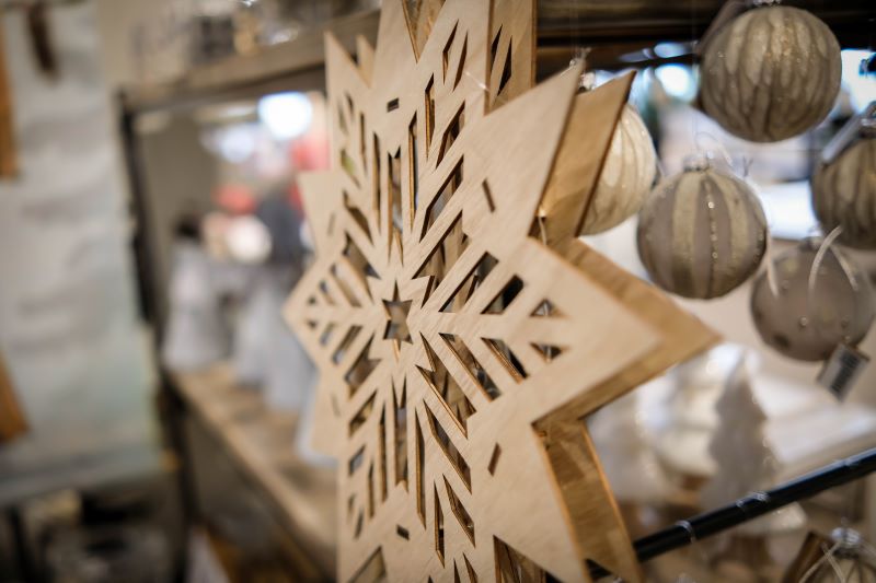 Nahaufnahme eines dekorativen Holzsterns vor einem Regal mit Weihnachtskugeln im Hintergrund