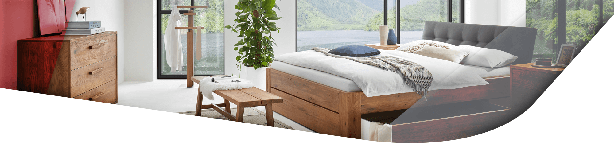 Hasena Bett, bei welchem ein Bettkasten integriert ist, welcher aktuell geöffnet ist. Im Hintergrund stehen die passenden Accessoires und Kommoden aus der Hasena Kollektion.