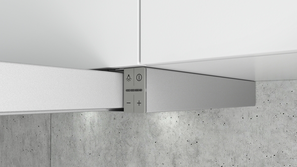 Detailansicht einer modernen Unterbau-Dunstabzugshaube mit LED-Beleuchtung, eingebaut in eine weiße Kücheneinrichtung über einer grauen Betonwand.