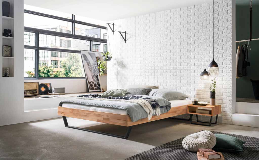 Hasena Trento - Bett Ostino | Kernbuche natur, geölt Helles Schlafzimmer mit einem Holzbett, weißen Backsteinwänden, großen Fenstern und stilvollen Dekorationen